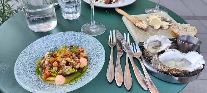Elegant utomhusmåltid med räkor, aioli, krutonger, ostron, smör, bröd och vinägrett på en somrig terrass.
