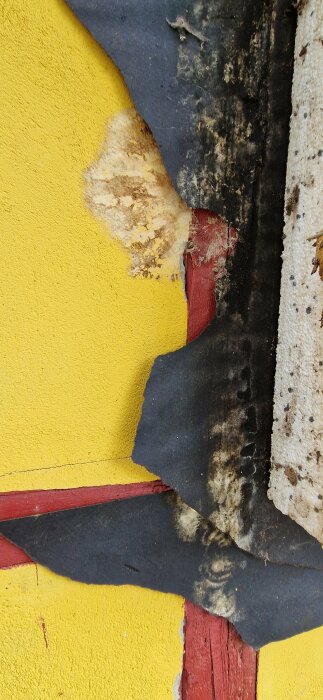Sliten yta med skadad svart matta, gul vägg, röda detaljer och synlig struktur, texturkontrast, förstörelse och nötning.