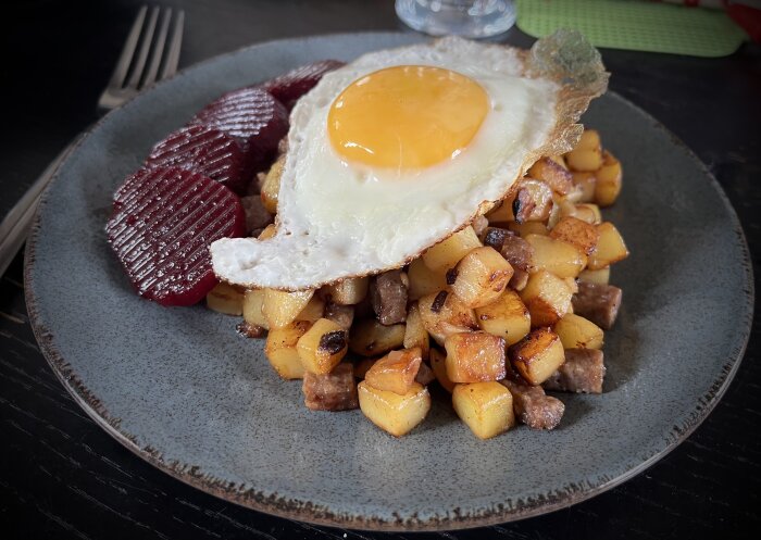 Pytt i panna med stekt ägg och rödbetor på blågrå tallrik, traditionell svensk maträtt, hemlagad.