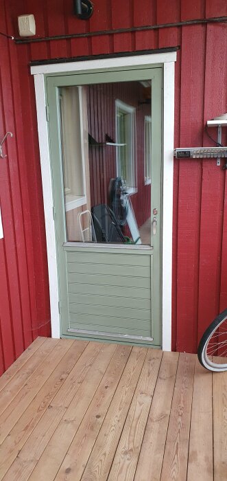 Röd trästuga, grönt fönster, veranda, reflektion hund i glas, cykelhjul, kabelrulle, vägglampa, infra-panel.