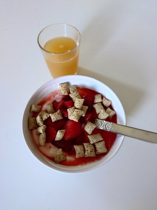 Frukostskål med yoghurt, jordgubbar, flingor och ett glas juice. Enkel, hälsosam måltid. Vit bakgrund.