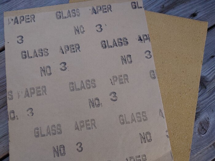 Två ark sandpapper med "GLASS PAPER NO 3" text stämplad, på träbord.