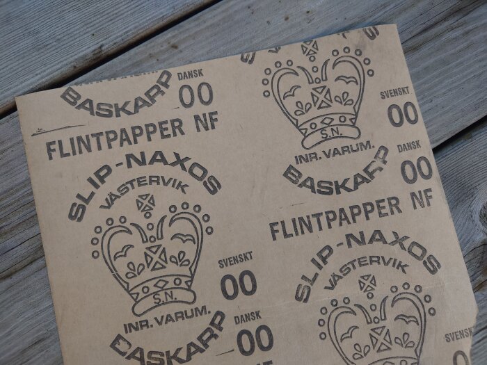 Brun papper med svart text och kungakrona, sannolikt förpackningsmaterial, antydan till Svensk-Dansk produkt.