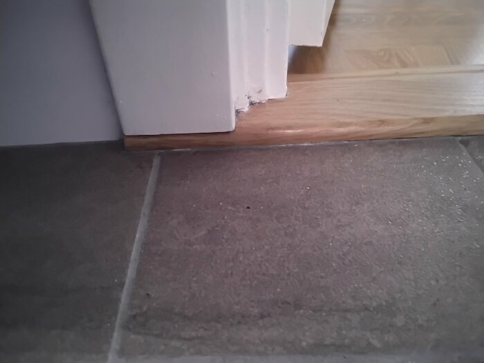 Dörrkarm, skadad list, stenplattor, trästeg, interiör, heminredningsskada, övergång mellan golvytor.