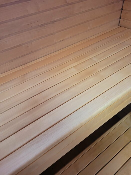 Träpaneler inne i en bastu, med horisontella sittbänkar och vertikala väggpaneler. Warm färgton.