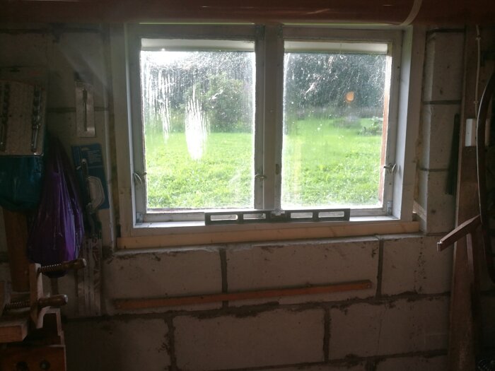 Ett fönster i en verkstadslokal visar en regnig dag ute.