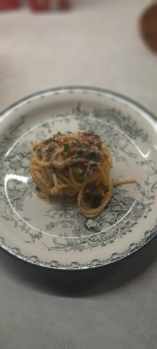 Spaghetti på dekorativ tallrik, med sås, strösslad parmesan, persilja, skarpt fokus på främre delen, suddig bakgrund.