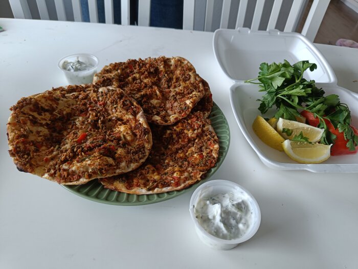 Turkisk lahmacun på tallrik, persilja, citron, tomat, tzatziki, på ett vitt bord.