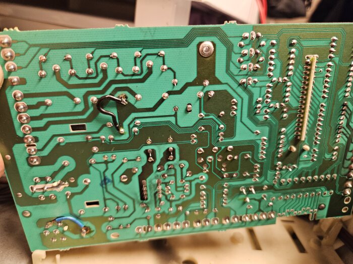 Kretskort bakifrån med lödpunkter, ledningar och kontaktstift. Elektronik, grönt, metall, kretsmönster, ingen monterad komponent.