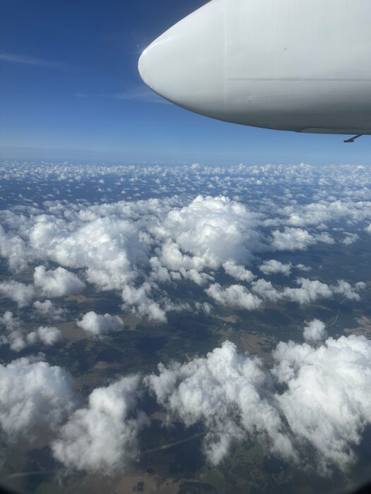 Flygplansvinge, utsikt över moln och landskap från ovan i dagsljus.