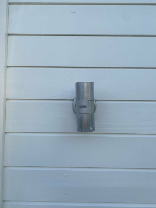 Metallventil eller röranslutning på en ljus sidovägg av hus, enkel industriell installation utomhus.