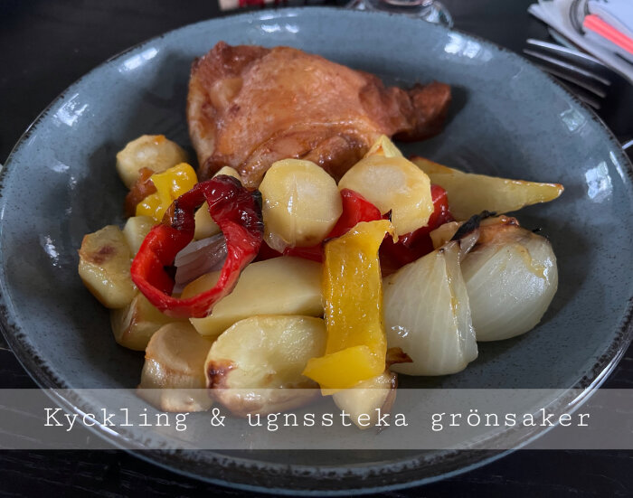 Stekt kycklinglår med potatis, röda och gula paprikor, lök på grå tallrik. Text: Kyckling & ugnstekta grönsaker.