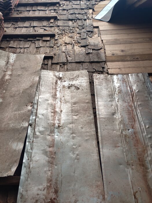 Nötta träplankor, fragmenterade takpannor och rostiga metallplåtar bildar en sliten fasad.