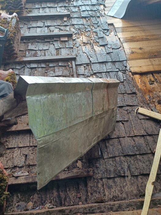 Föråldrat tak med skadade shingelplattor, mossa, träförfall och metallkant, under reparation eller utbyte.