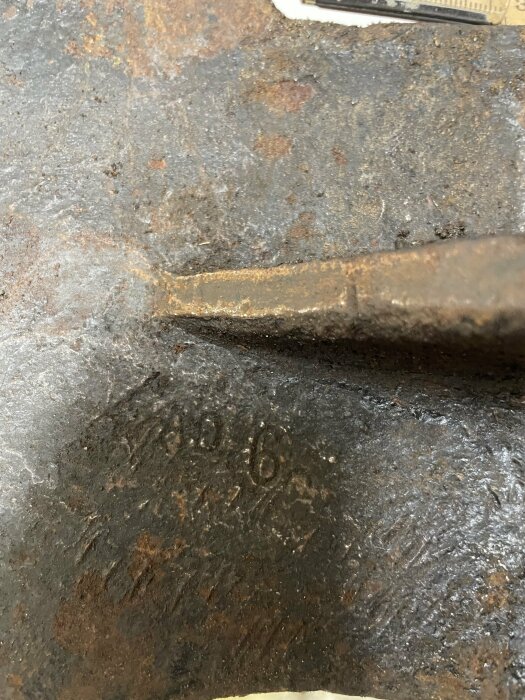 Närbild på sliten yta med siffror "1396" präglat i metallen. Rustik och grov textur, möjligen en del av verktyg.