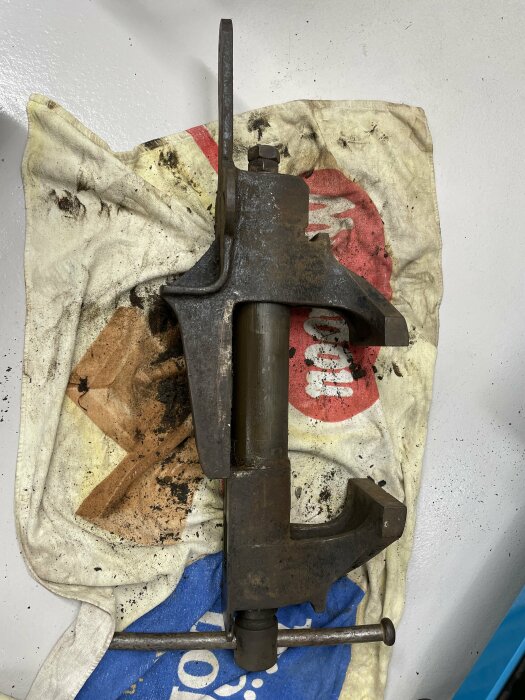 En smutsig skruvstycke på en fläckig trasa, verktyg för fastspänning, industrisyfte, ligger mot en vit vägg.