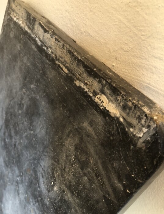 Snedbild av svart, slitet hörn nära en vit vägg, med damm och repor.