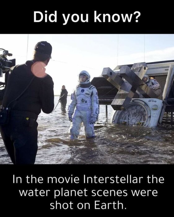 Filmproduktion vid vatten med skådespelare i rymddräkt, text om "Interstellar". Filmkameror, personal och utrustning synliga.