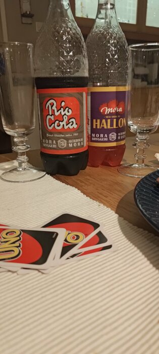 Två läskflaskor, glas, Uno-kort och tallrik på ett bord.