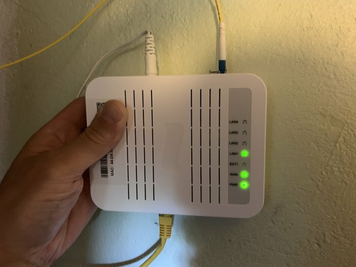 En hand håller en vit router med lysande lampor på en vägg.