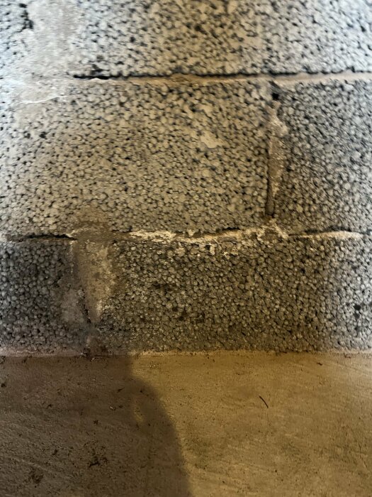 Slitna, grå betongblock. Skugga nedtill. Smutsiga fogar. Grov yta. Detalj av vägg eller grund.
