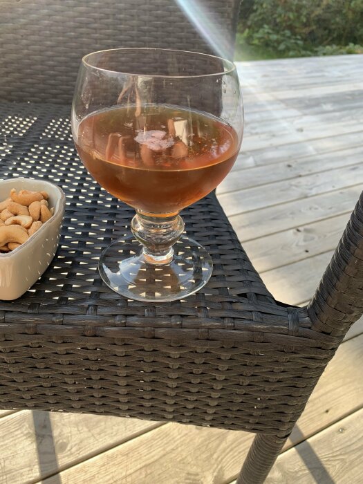 Färgat dryck i glas med is på rottingbord utomhus, skål med snacks bredvid, trädäck i bakgrunden.
