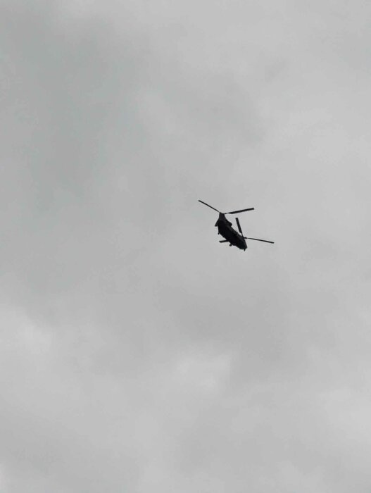 Helikopter flyger genom molnig himmel. Ensilhouette mot ljusgrå bakgrund.