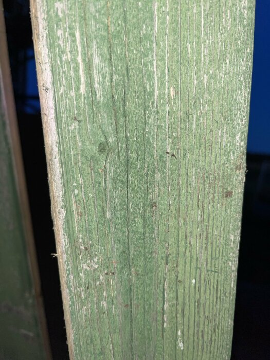 Grönmålad träyta med slitage, närbild, vertikala linjer och textur, möjligtvis en del av en stolpe.