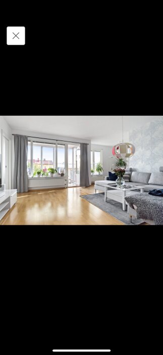 Ljus vardagsrum, modern inredning, trägolv, stora fönster, grå soffa, vitmöbler, balkongdörr, växttapet, dekorativ belysning, skandinavisk stil.