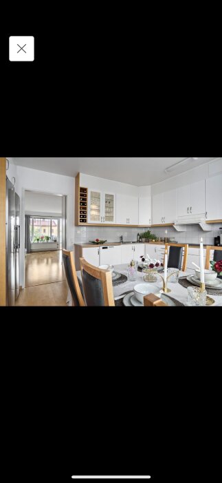 Modernt kök med vit skåpinredning, rostfria vitvaror, dukat matbord, trägolv och öppen planlösning.