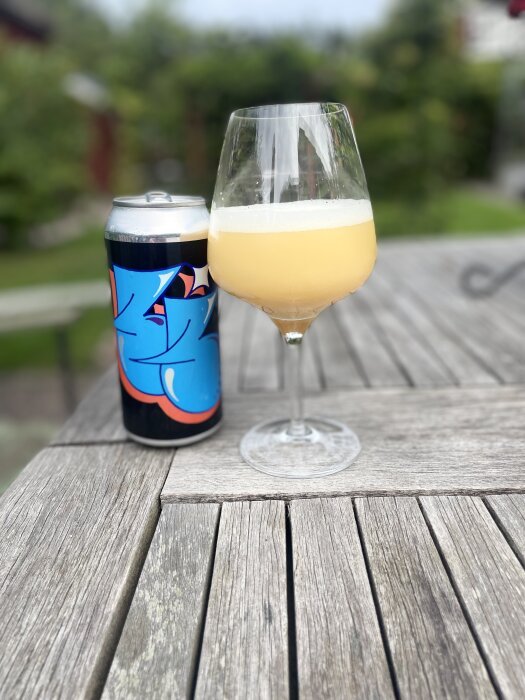 Ölburk med färgrik design och ett glas med skummande öl på träbord utomhus.