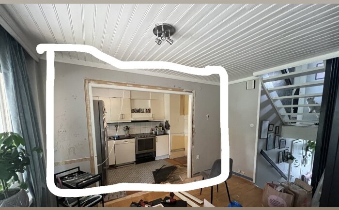 Inomhusmiljö under renovering, öppen planlösning, kök, sällskapsrum, vitmålade takbjälkar, trappa och inredningsdetaljer synliga.