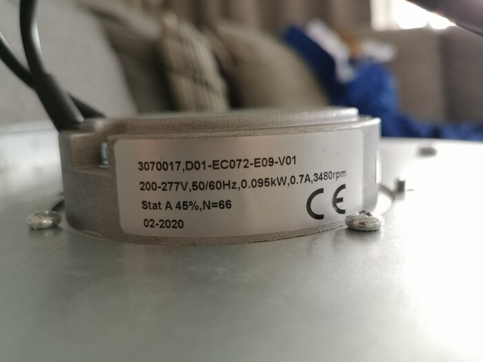 En elektrisk motor med etikett, specifikationer, CE-märkning, suddig bakgrund med kablar och tyg. Daterad 02-2020.