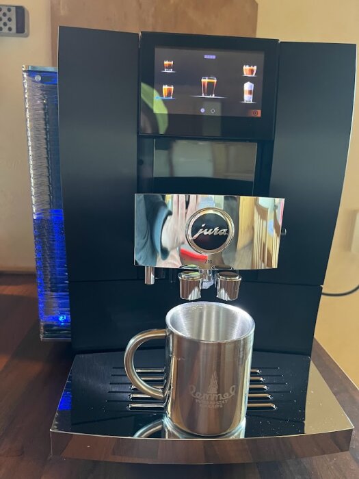Espressomaskin, digital display, metallmugg, vattenbehållare, modern köksapparat, bänkskiva, rostfritt stål.