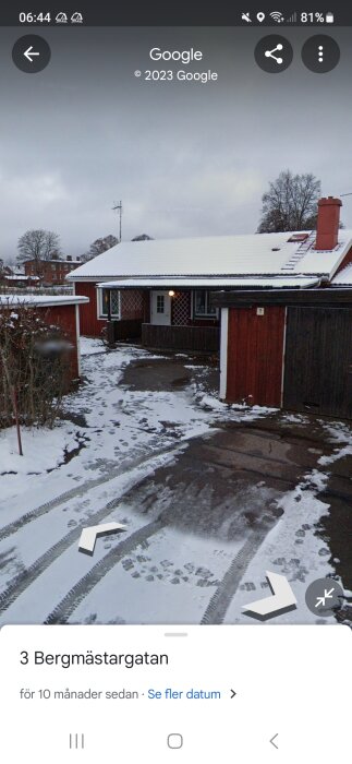 Ett rött hus med snötäckt tak, gatuvy, vinter, fotspår och bildspår på marken.
