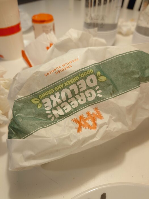 En oöppnad förpackning med snabbmat, pappersmuggar och en tallrik i bakgrunden, ligger på bord.