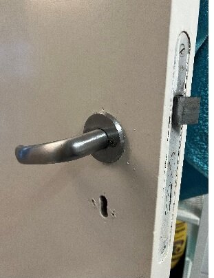 Dörrhandtag i silverfärg med låskista, på öppen vit dörr, närbild.