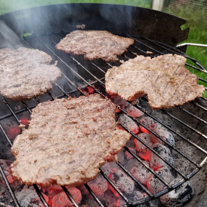 Hamburgare grillas på kolgrill, rök synlig, utomhusaktivitet, sommartid, avslappnad matlagning.