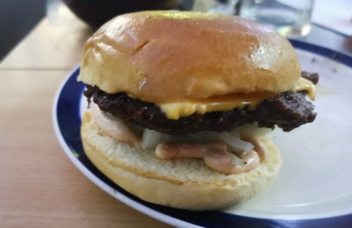 Hamburgare med kött, ost, lök och sås på vitt tallrik. Nahaft, enkel, snabbmat, gulbrunt bröd.