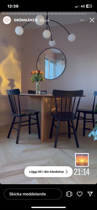Ett modernt matsalsrum med rund spegel, lampa med flera kulor, träbord, stolar och en vas rosor.