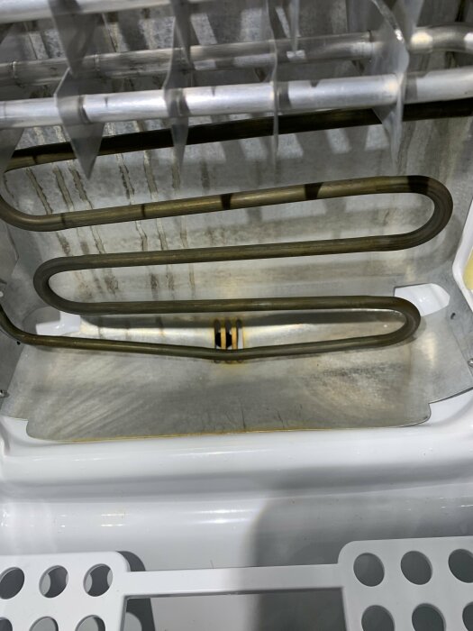 Interiör av öppen diskmaskin, nedre korg, värmeelement synligt, smutsiga fläckar, behöver rengöring.