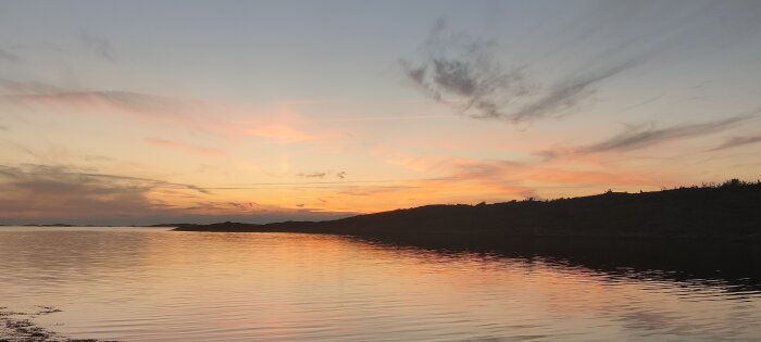 Solnedgång vid havet, spegelblank vattenyta, orange himmel, moln, kustlinje, lugnt, skönhet i naturen.