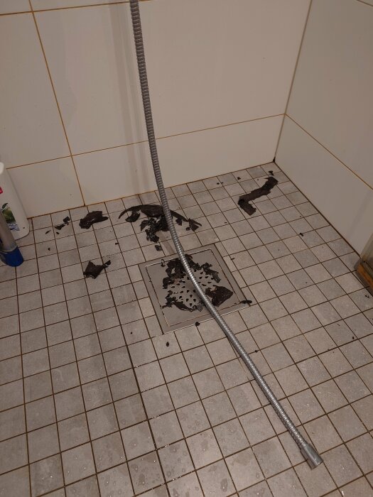 Golvbrunn i badrum med igensatta hår och skräp, behöver rengöring och underhåll.