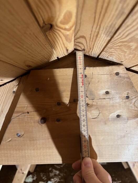 Mätning av träkonstruktionens innerhörn med tumstock. Träbjälkar. Konstruktionsdetalj. Hantverk. Skuggor på ytan.