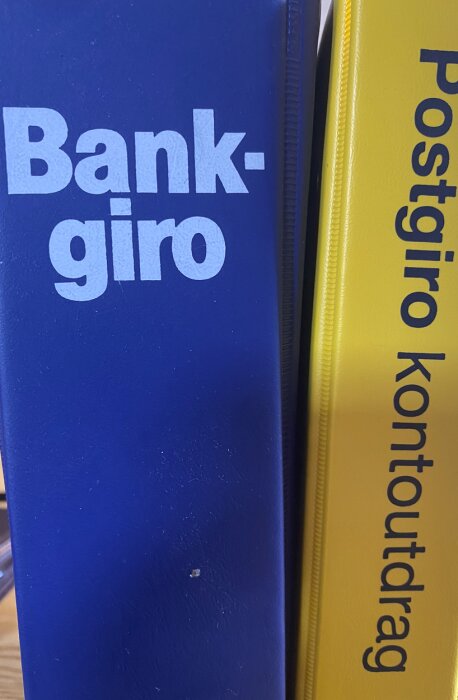 Blå och gul pärm med texten "Bankgiro" och "Postgiro kontoutdrag", antyder finansiella dokument eller arkivering.