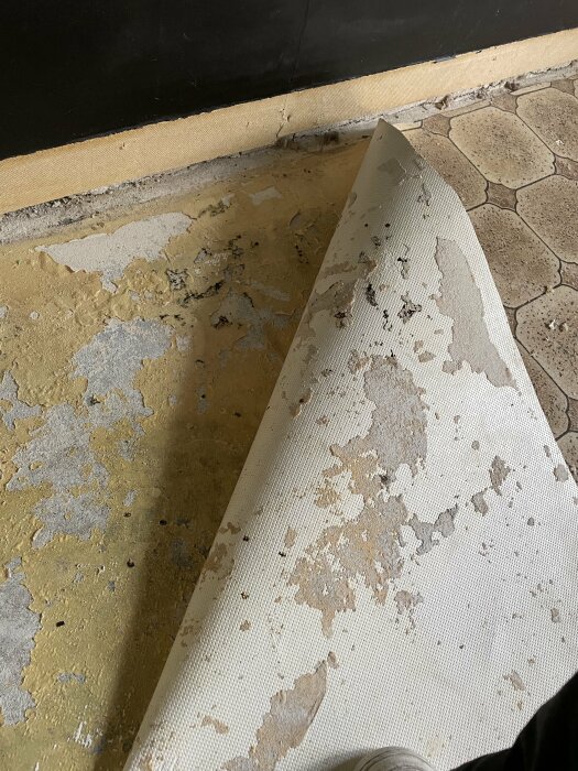 Slitet golv med uppvikta hörn och färgflagnande mönster, behöver renovering eller utbyte.