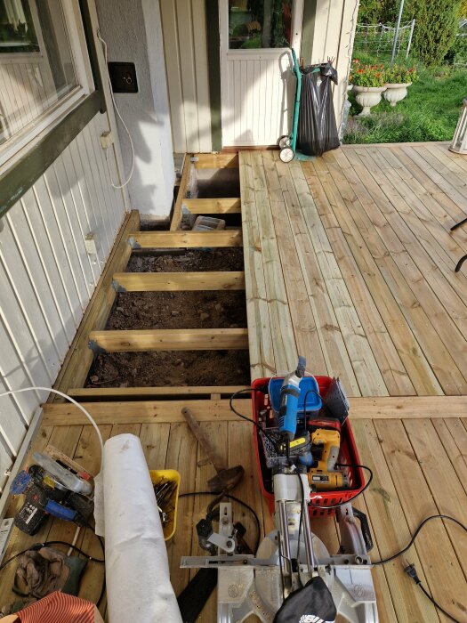 Reparationsarbete på träaltan, verktyg och material på plats, öppnat golvavsnitt visar stödstruktur.