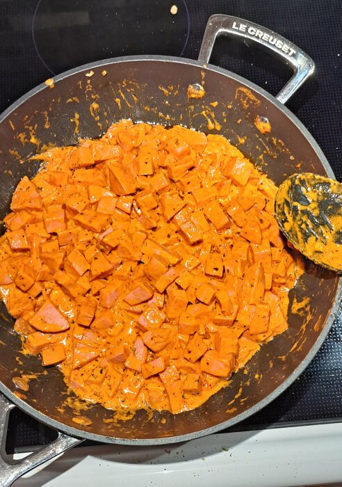 Stekt sötpotatis i kryddig sås i gjutjärnspanna, grytspade, matlagning, köksmiljö.