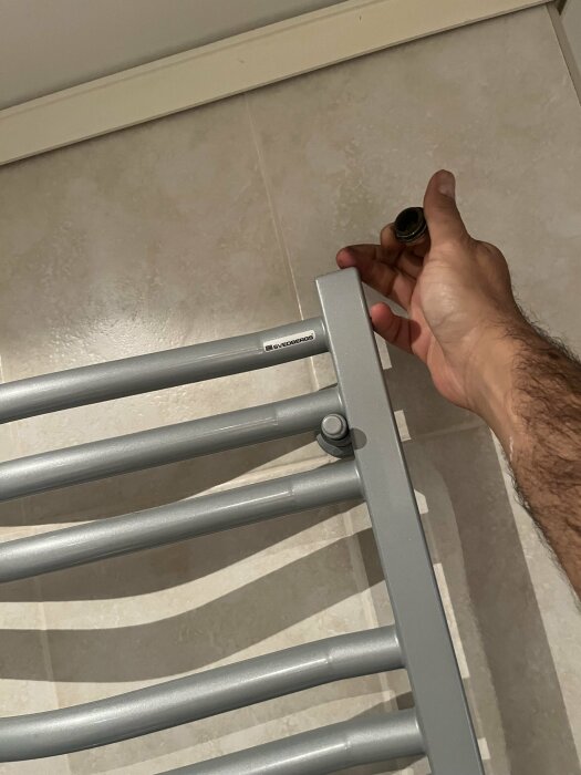 En person håller en avtagen knopp från en uppfälld handdukstork i ett badrum.