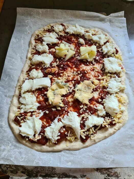 Ogräddad pizza med tomatsås, flera ostar, ligger på bakplåtspapper.